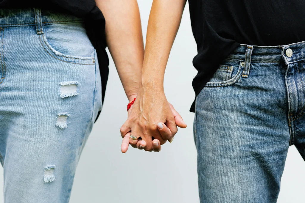 Close-up of couple holding hands wearing black tops and distressed denim jeans, showing wedding rings and symbolizing connection, commitment, and everyday relationship moments after the woman was asking herself "is my boyfriend gay"