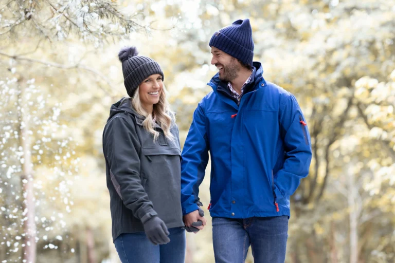 Happy couple in winter jackets holding hands while hiking on affordable vacation in nature