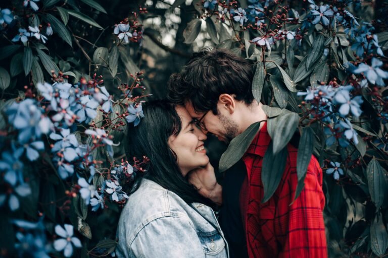 Romantic couple poses with forehead touch at their wedding anniversary wishes for couple while surrounded by blue flowers demonstrating intimate natural photography position
