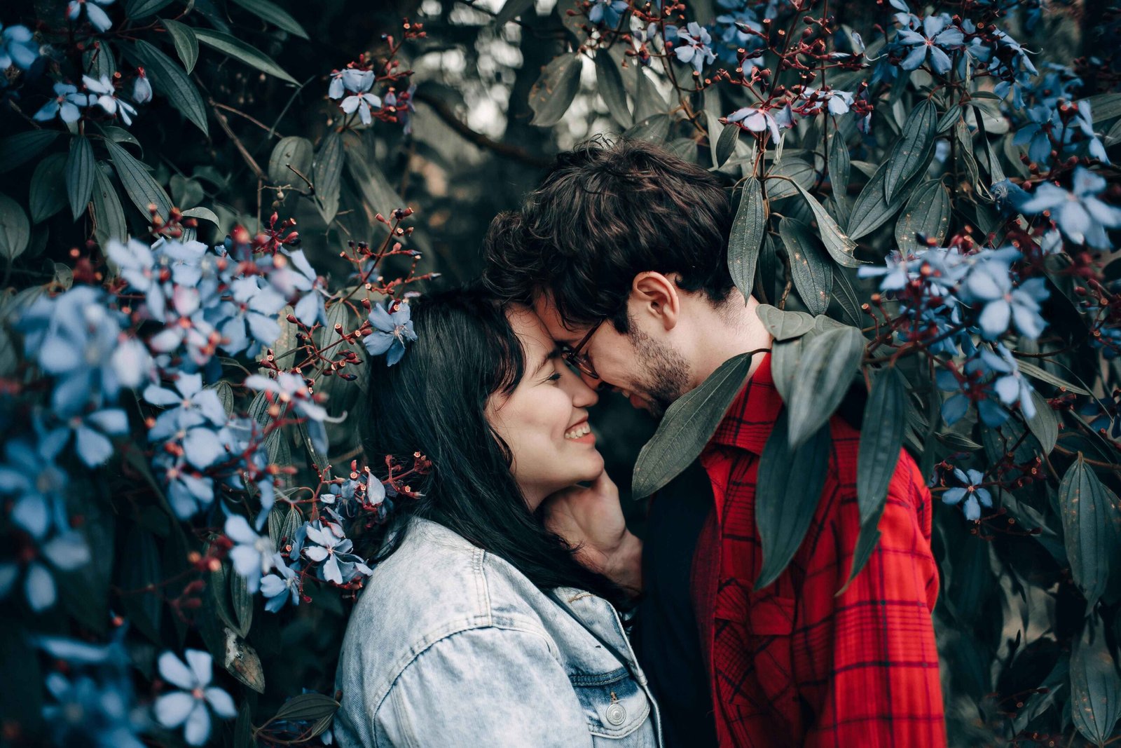 Romantic couple poses with forehead touch at their wedding anniversary wishes for couple while surrounded by blue flowers demonstrating intimate natural photography position