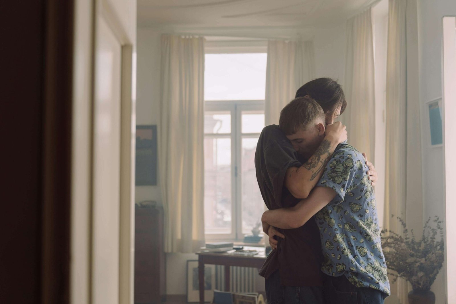 Couple in emotional embrace standing by window in bright room, showing comfort, support, and deep emotional connection during intimate moment together