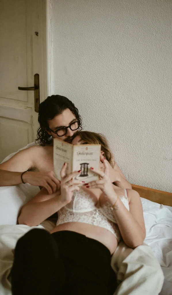 A couple relaxing together on a bed while reading, representing intimacy, communication, and exploring whether is asking about a person's sexual preferences unhealthy behavior in relationships.