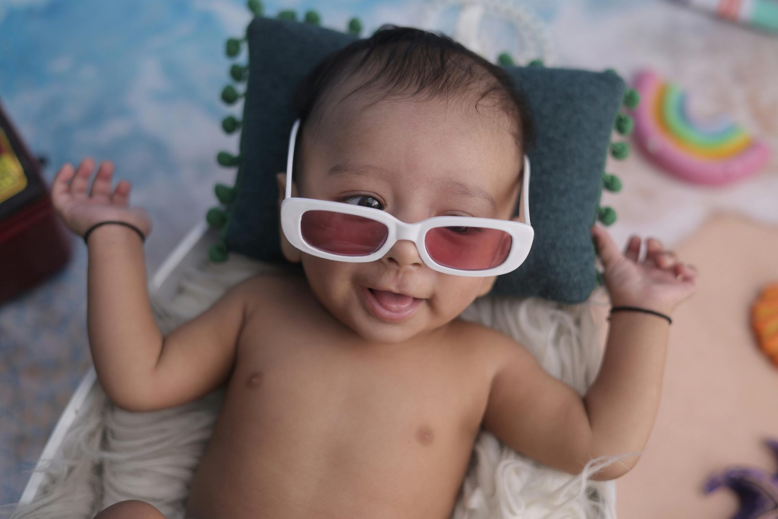 Smiling baby lying down wearing sunglasses, related to milestones like when do toddlers start talking